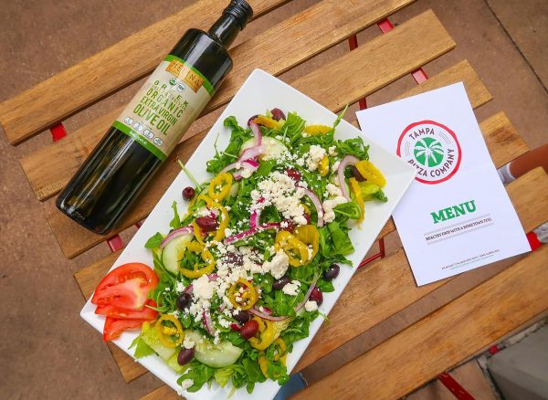 Bottle of Melina Extra Virgin Olive Oil next to a salad with olives and peppers